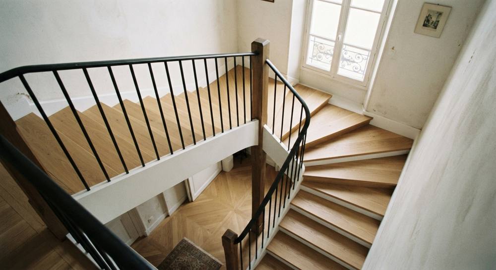 Vue plongeante sur le virage d'un escalier quart tournant en chêne avec marches balancées et garde-corps métallique noir