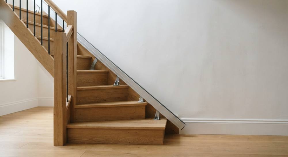 Bas d'un escalier en chêne avec un rail de monte-escalier en aluminium fixé sur le bord des marches par des pieds de support métalliques